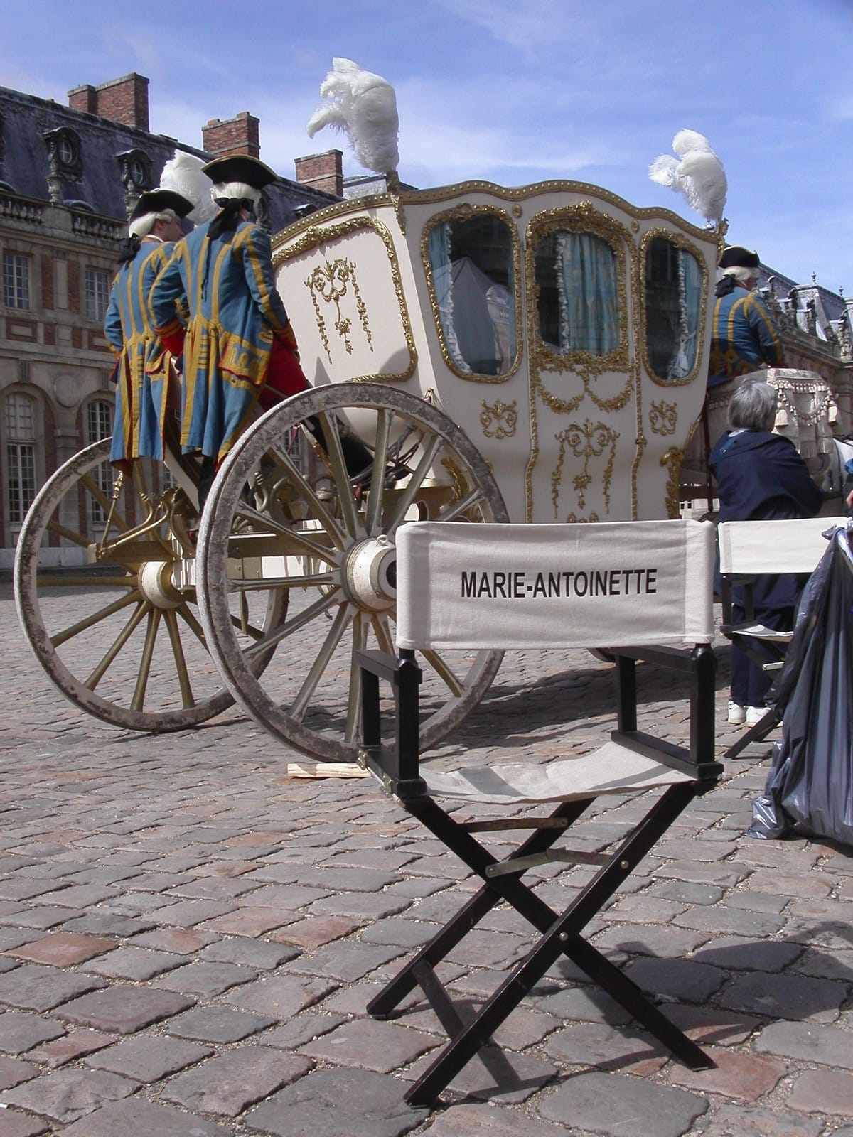 Chaise de réalisatrice marquée Marie-Antoinette devant le carrosse royal dans la cour du château de Versailles pendant le tournage