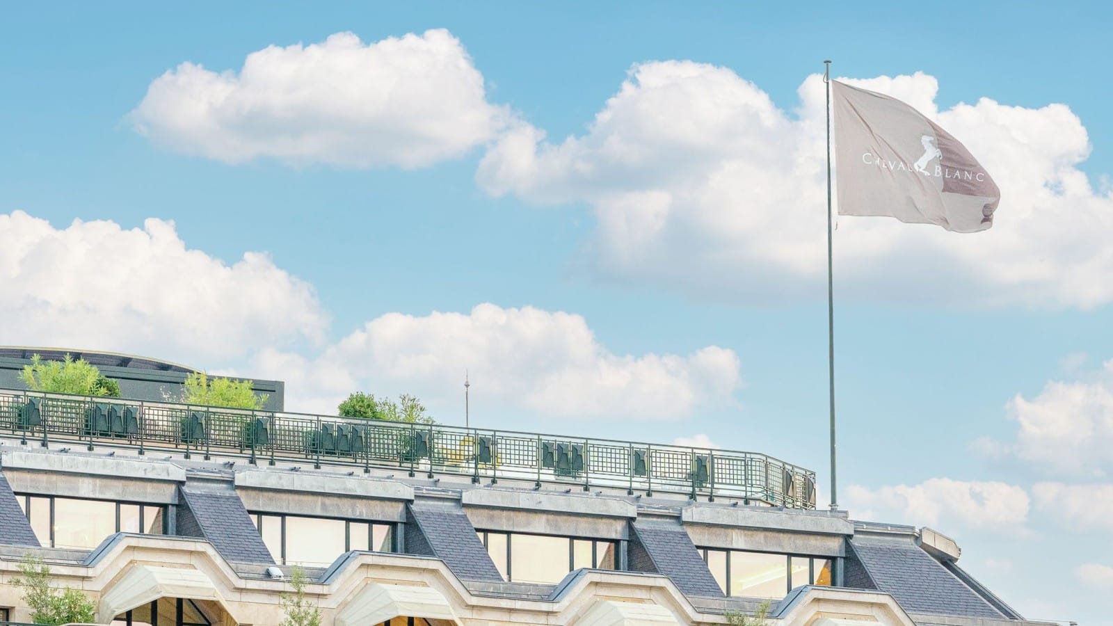 Un pavillon blanc portant le monogramme Cheval Blanc flotte au vent au sommet du toit de l’ancien bâtiment de la Samaritaine, à Paris, sous un ciel de nuages.