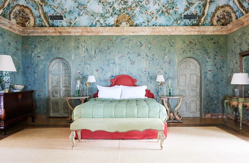 Une chambre de The Terraces : décor végétal peint, lit à tête rouge, plafond ouvragé. Le catalogue expose le luxe intérieur que le tarif propose à la location.