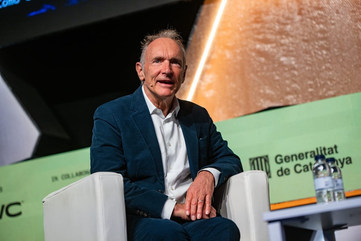 Tim Berners Lee assis dans un fauteuil blanc sur la scène du Talent Arena à Barcelone, micro casque, veste bleue, devant un fond vert Generalitat de Catalunya