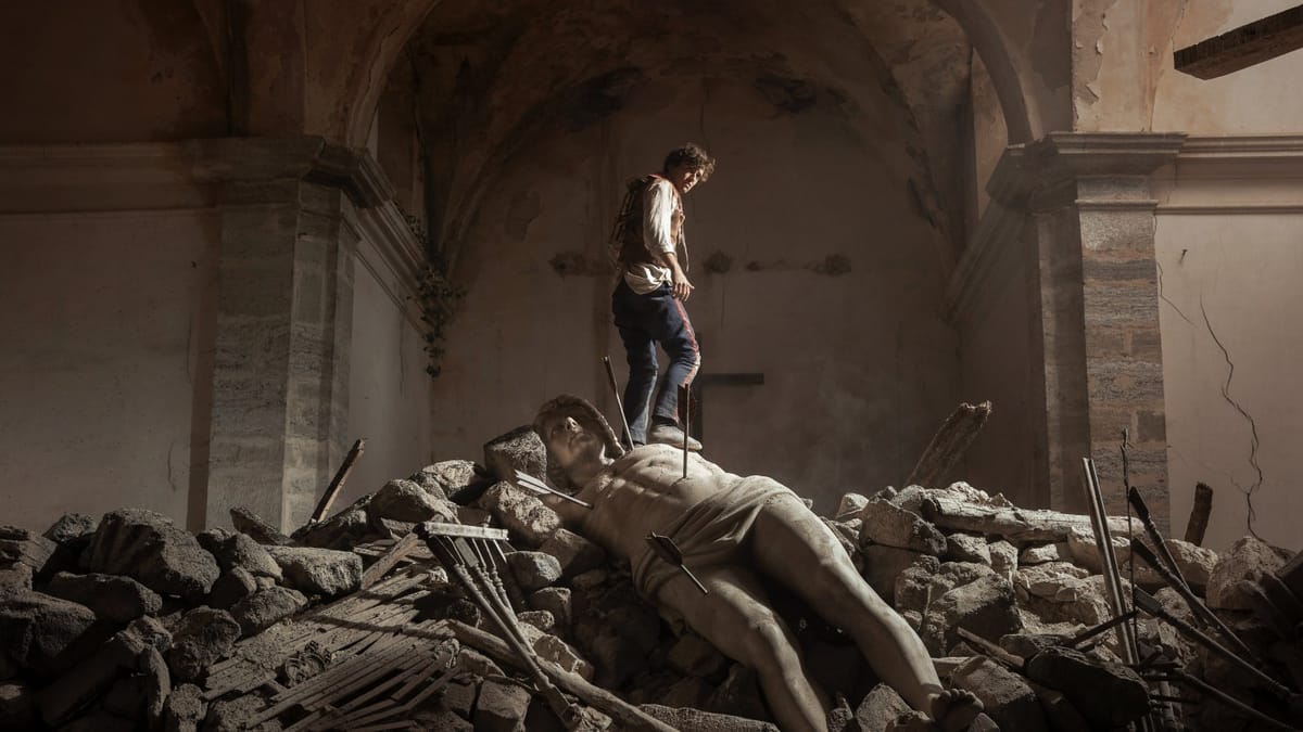 Un jeune homme debout sur une statue renversée au milieu des gravats d’une église en ruine