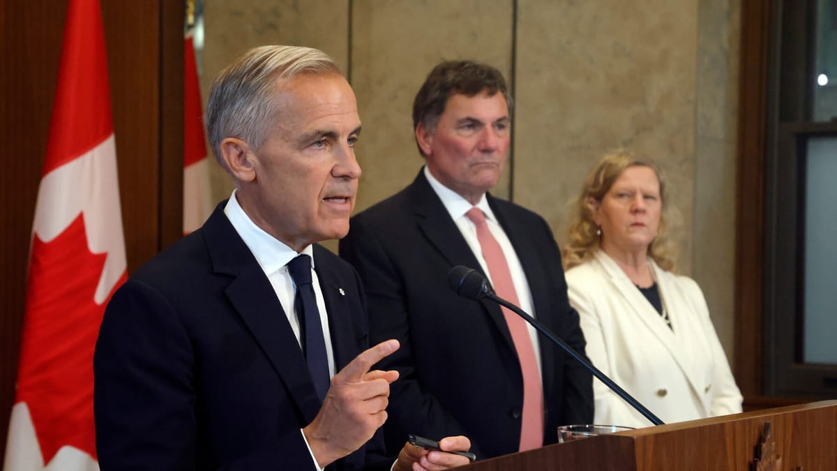 Mark Carney parle au pupitre, index levé, deux membres du gouvernement derrière lui et un drapeau canadien à gauche