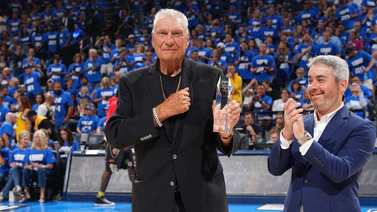 Don Nelson, cheveux blancs et veste noire, tient le trophée Chuck Daly sur un parquet NBA devant une tribune remplie de spectateurs en maillots bleus