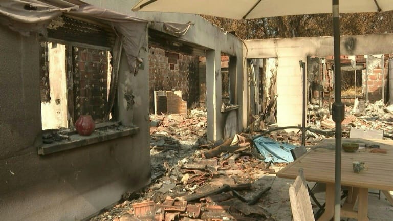 Intérieur d’une maison détruite par l’incendie en Gironde, murs noircis, toiture effondrée, table de jardin et parasol intacts au premier plan