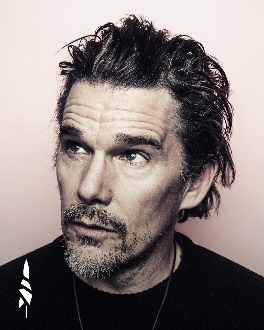 Portrait en noir et blanc teinté de l’acteur Ethan Hawke, le regard levé de côté, pull sombre, sur fond clair.