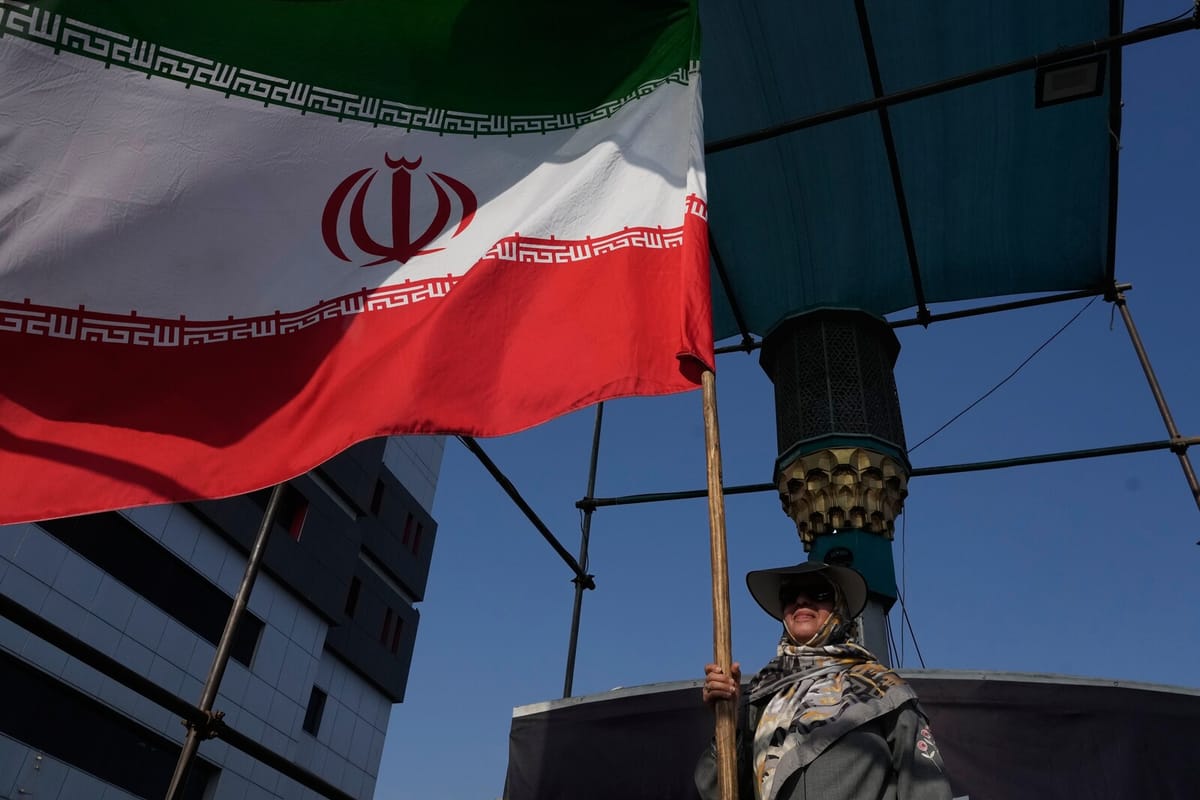 Une femme portant un chapeau et un foulard tient un mât surmonté d’un grand drapeau iranien lors d’un rassemblement dans le centre de Téhéran