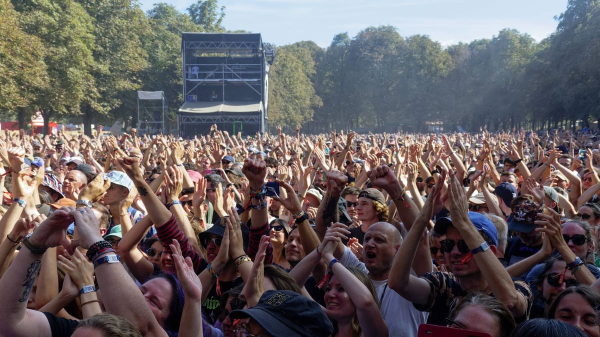 Foule dense de festivaliers bras levés et mains tendues devant la Grande Scène de Rock en Seine, en plein jour, entourée d’arbres du Domaine national de Saint-Cloud.