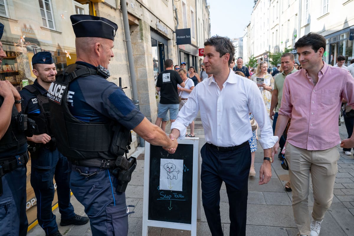 Gabriel Attal serre la main d un policier municipal dans une rue piétonne, entouré de passants, en été