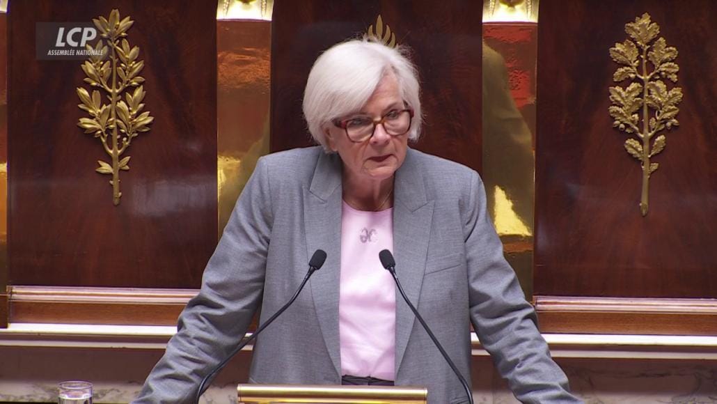 Catherine Vautrin, ministre des Armées, s’exprime derrière deux micros à la tribune de l’Assemblée nationale, devant les panneaux dorés de l’hémicycle.