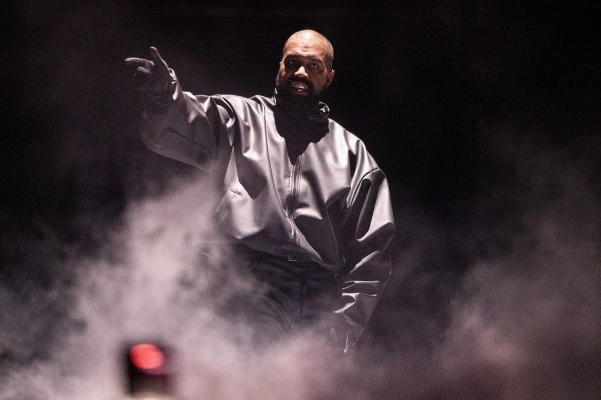 Ye, anciennement Kanye West, sur scène dans la fumée, bras tendu et index pointé, veste sombre en cuir.