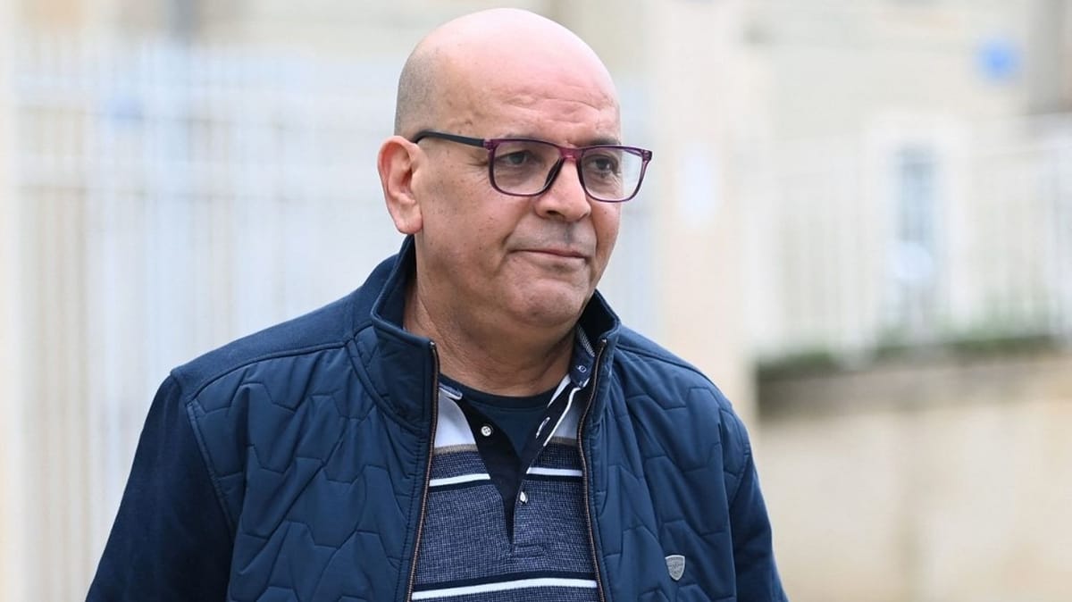 Boualem Naman, dit Doualemn, photographié de face en extérieur, veste matelassée bleu marine et lunettes