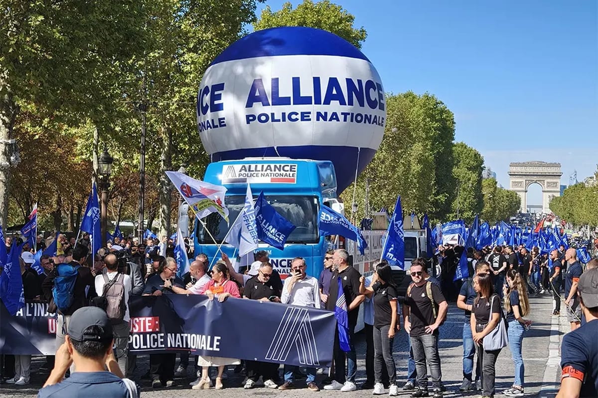 Cortège de policiers avenue des Champs-Élysées derrière un ballon gonflable Alliance Police Nationale, l’Arc de Triomphe visible au fond