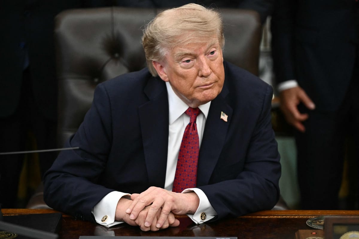 Donald Trump, mains jointes, assis derrière le bureau du Bureau ovale de la Maison Blanche.