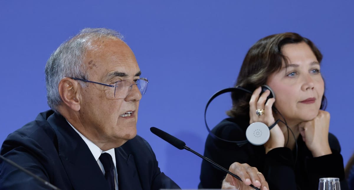 Alberto Barbera parle au micro à la conférence de presse des jurys de la 83e Mostra, Maggie Gyllenhaal à sa droite, une oreillette de traduction contre l’oreille, le menton sur la main.